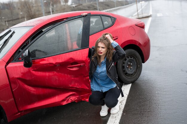 La mujer se sienta cerca de un coche averiado después de un accidente. llamar por ayuda. seguro de auto