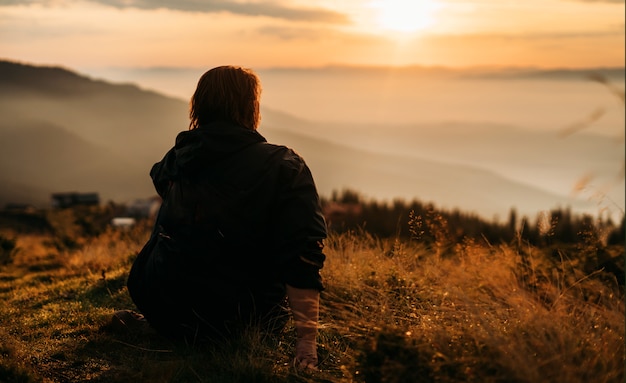 Una mujer se sienta en la cima de una montaña esperando que salga el sol.
