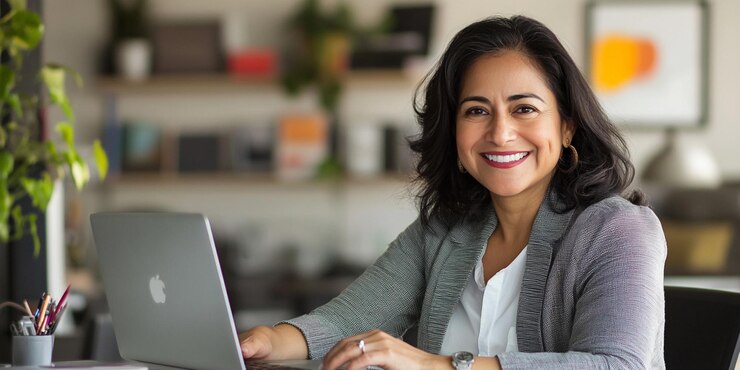 una mujer se sienta en un escritorio con una computadora portátil y sonriendo