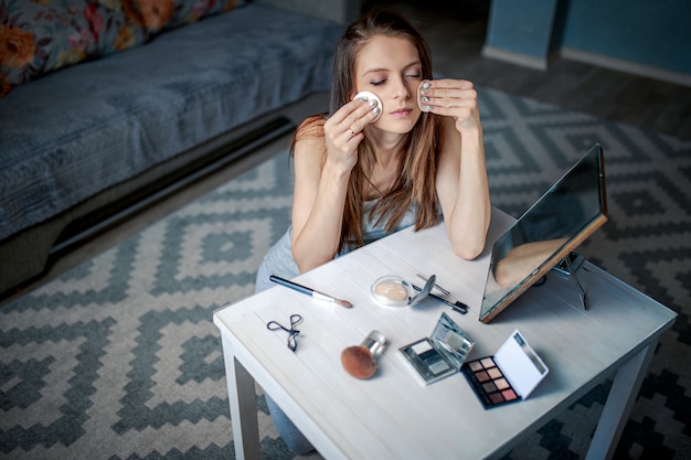 La mujer se sienta ante el espejo con esponjas en las manos. Mujer haciendo maquillaje