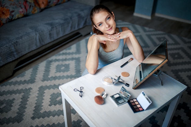 La mujer se sienta ante el espejo y sonríe. Mujer haciendo maquillaje