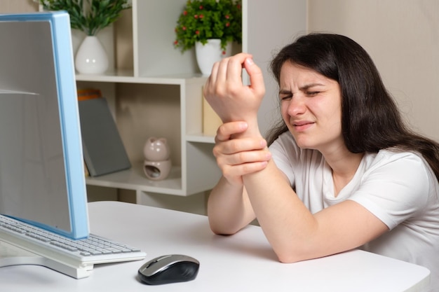 Una mujer se sienta frente a una computadora y se lleva la mano a la muñeca.