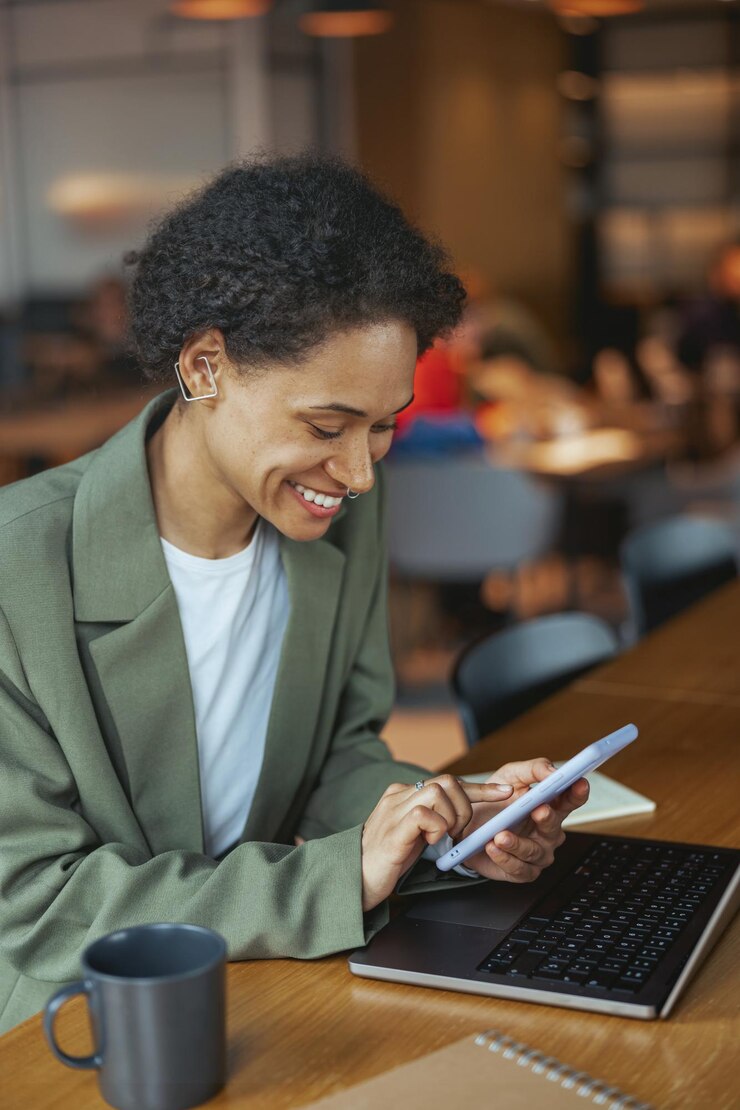 Foto una mujer se sienta en una mesa con una computadora portátil y una tableta sonriendo en su blazer