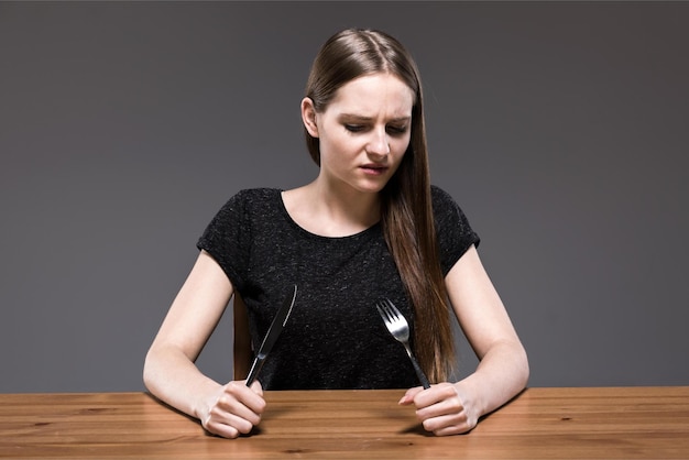 Una mujer se sienta en una mesa con un cuchillo y un tenedor en la mano.