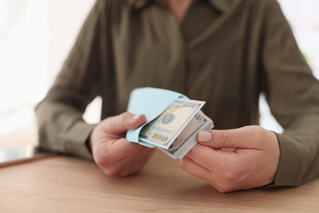 La mujer se sienta a la mesa y sostiene un sobre con una pila de billetes de un dólar concepto de ganancias