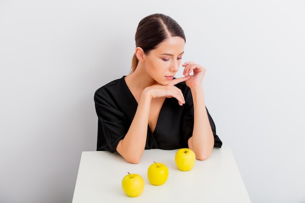 La mujer se sienta a la mesa con tres manzanas amarillas