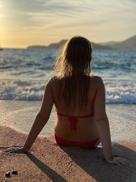 Una mujer se sienta en una playa frente a una puesta de sol.