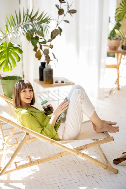 La mujer se sienta relajada con una bebida en la habitación con plantas.