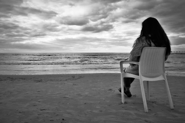Una mujer se sienta en una silla en la playa frente al mar.