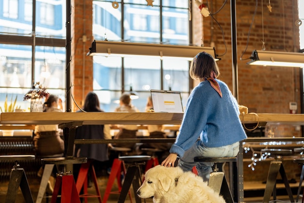 La mujer se sienta con su perro en la cafetería moderna