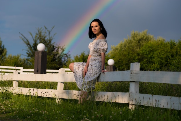 Una mujer se sienta en una valla frente a un arco iris.