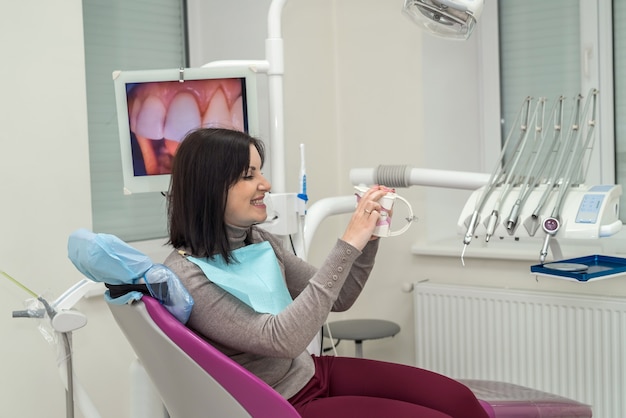 Mujer en silla de dentista sosteniendo la mandíbula y sonriendo