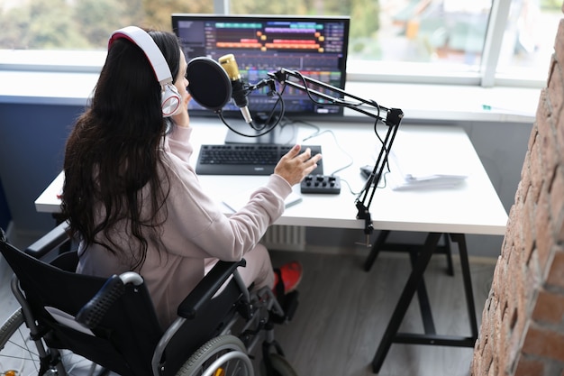 Mujer en silla de ruedas con auriculares habla por micrófono frente a trabajo de monitor de computadora