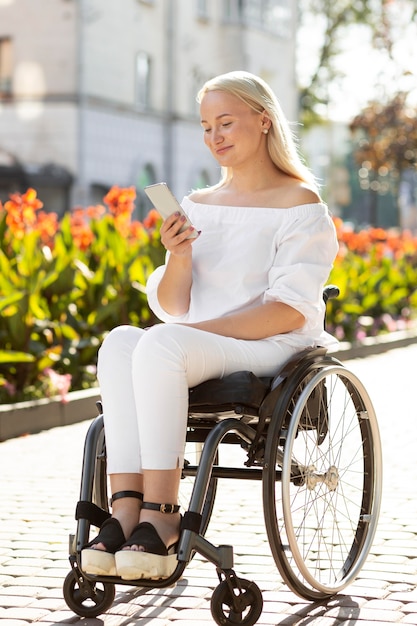 Foto mujer en silla de ruedas en la ciudad con smartphone