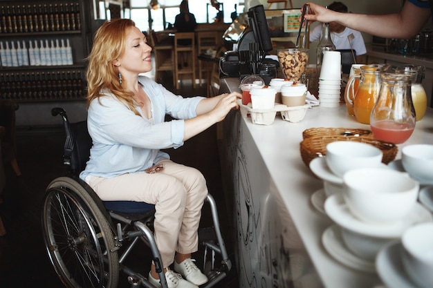 Foto mujer en silla de ruedas compra café y bollos en un café.