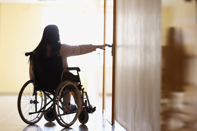 Mujer en silla de ruedas se extiende para abrir la manija de la puerta en el pasillo oscuro