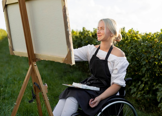 Mujer en silla de ruedas pintura en la naturaleza sobre lienzo