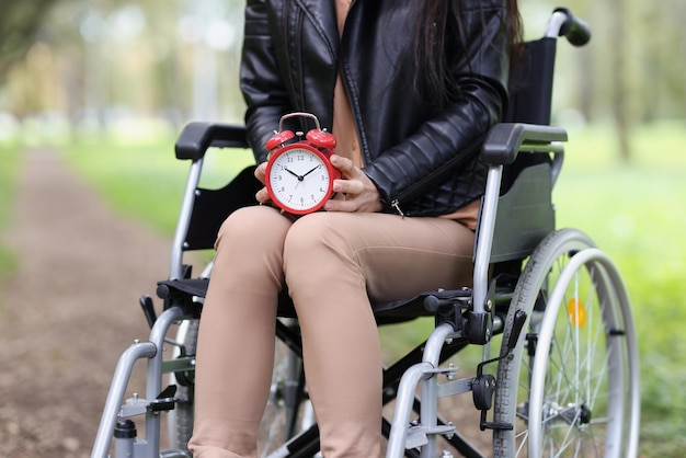Mujer en silla de ruedas sostiene despertador en tiempo de caminata en el parque y rehabilitación después de una lesión