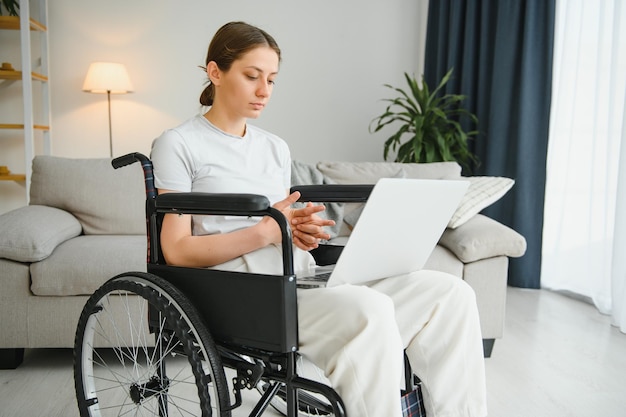 Mujer en silla de ruedas trabaja en la computadora portátil en la oficina en casa con un perro de asistencia como compañero