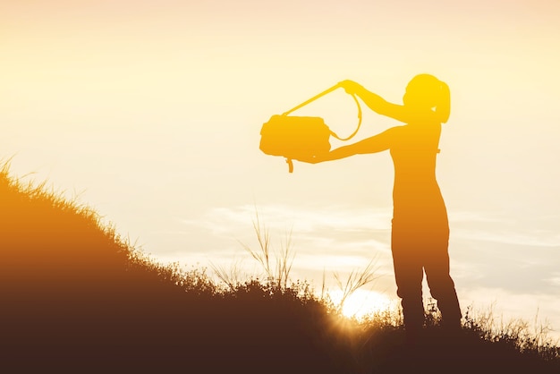 Mujer de silueta con una bolsa de cámara en un prado al atardecer