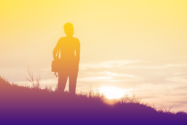 Mujer de silueta con una bolsa de cámara en un prado al atardecer