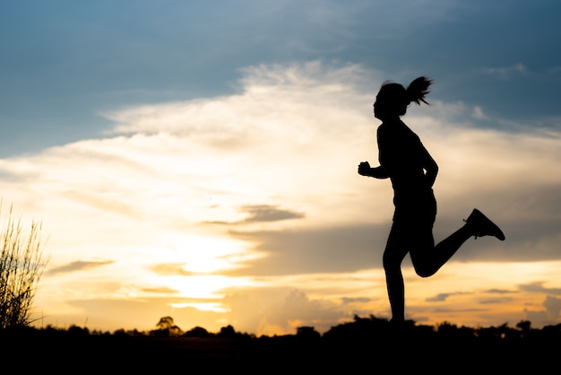 Mujer de silueta corriendo sola al hermoso atardecer en el parque.