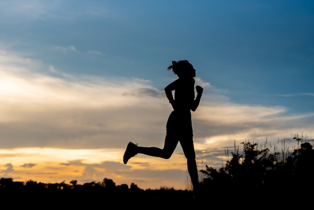 Mujer de silueta corriendo sola al hermoso atardecer en el parque.