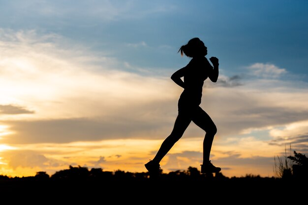 Mujer de silueta corriendo sola al hermoso atardecer en el parque.