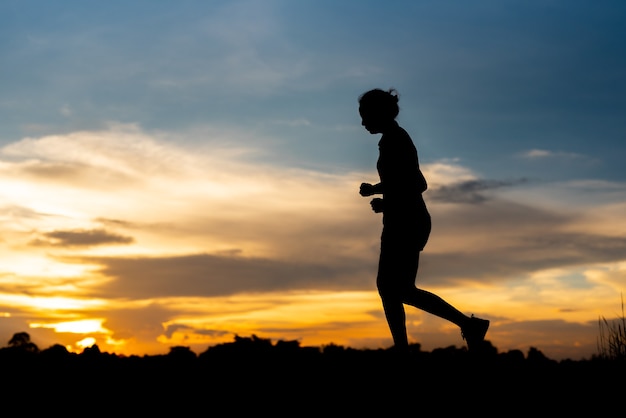 Mujer de silueta corriendo sola al hermoso atardecer en el parque.