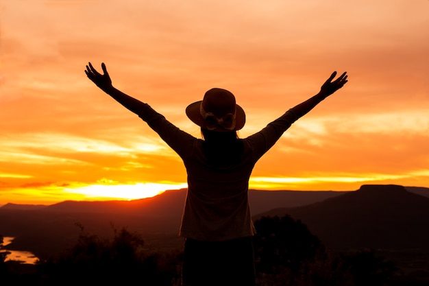 mujer de silueta se encuentra en la cima de la montaña al atardecer, libertad mujer feliz disfrutando de la puesta de sol ...