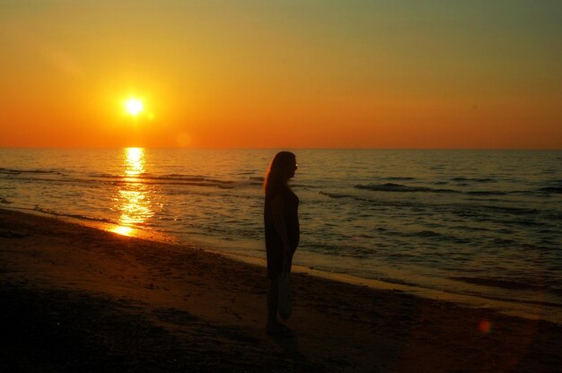 Foto mujer silueta de pie en la playa contra el cielo naranja