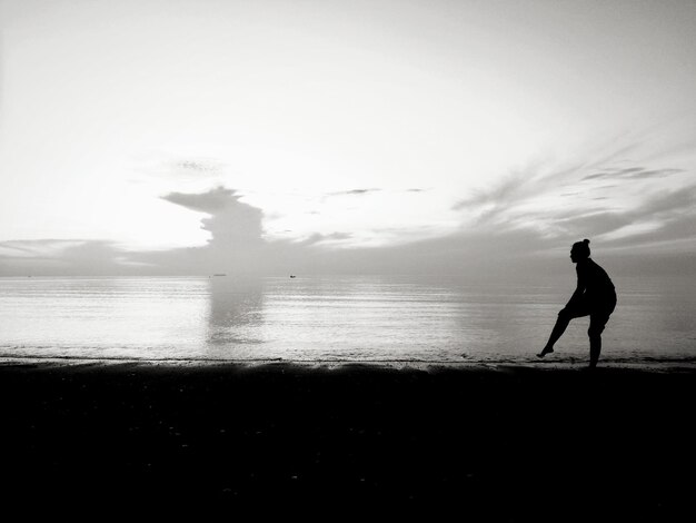 Foto mujer silueta de pie en la playa contra el cielo