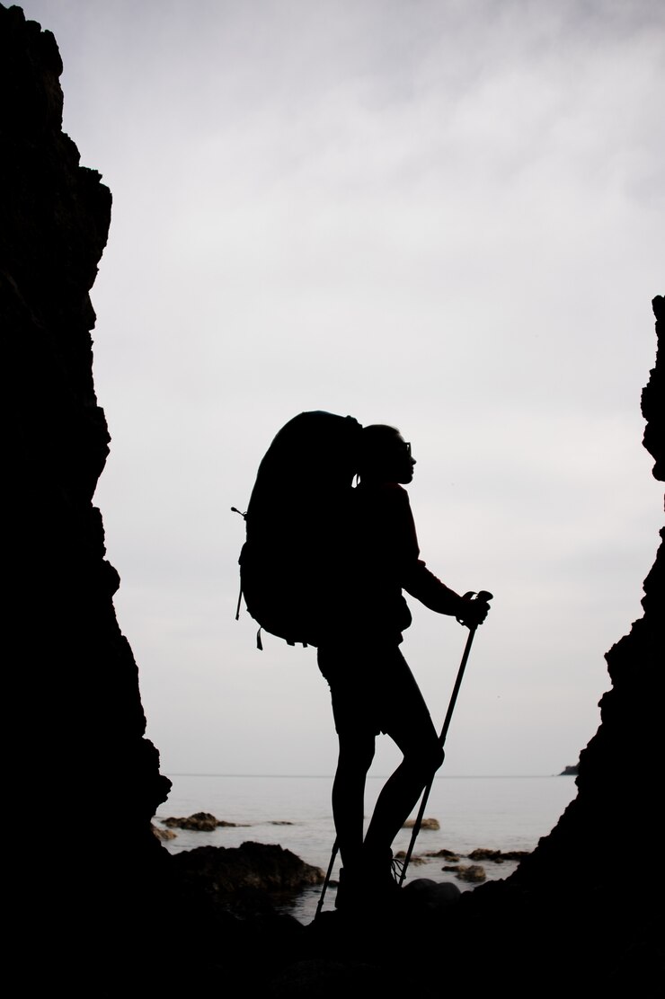 Foto mujer de silueta de pie entre las rocas en la costa en el mar con mochila de senderismo