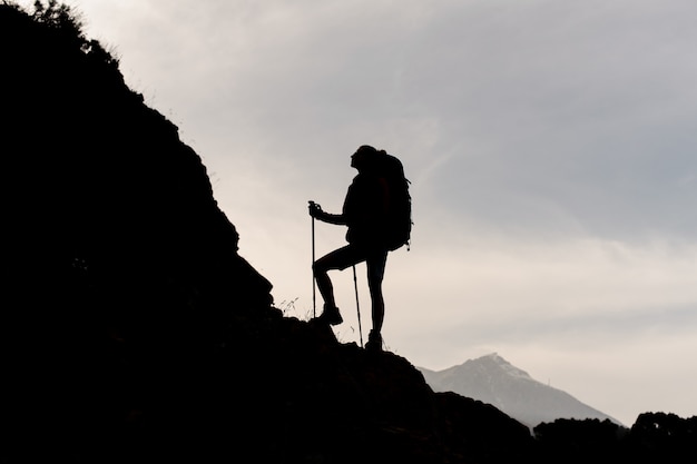 Mujer de silueta de pie sobre las rocas con mochila de senderismo y bastones