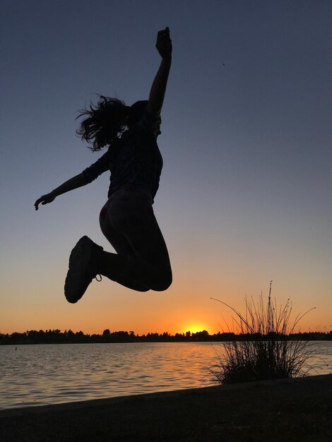 Mujer silueta saltando en la playa contra el cielo durante la puesta de sol