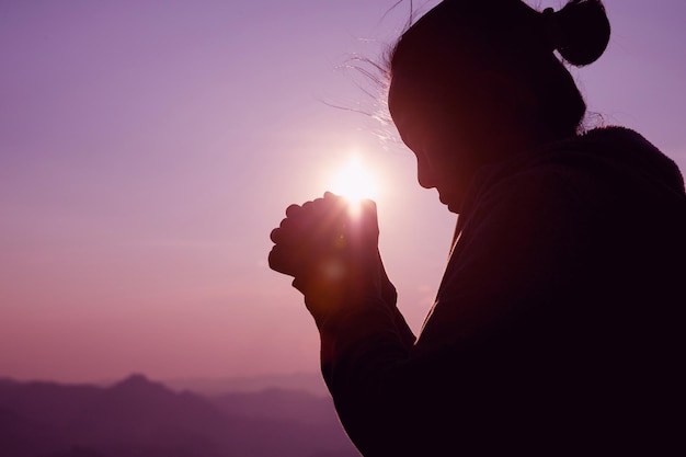 Mujer de silueta sobre fondo de puesta de sol. Mujer levantando sus manos en adoración.