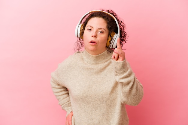 Mujer con síndrome de Down con auriculares aislados en pared rosa teniendo una idea, concepto de inspiración.