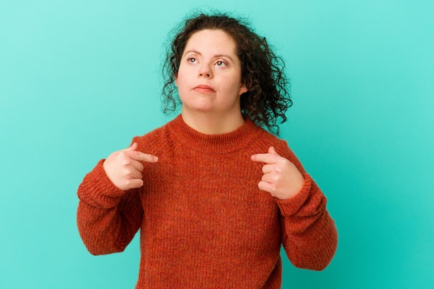 Foto mujer con síndrome de down persona aislada apuntando con la mano a un espacio de copia de camisa, orgulloso y seguro