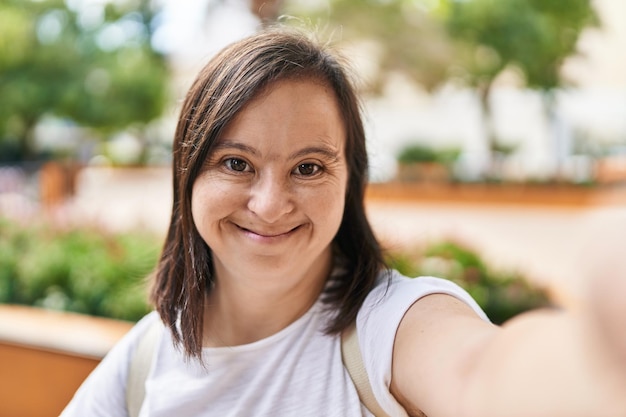 Mujer con síndrome de Down sonriendo confiada haciendo selfie junto a la cámara en el parque