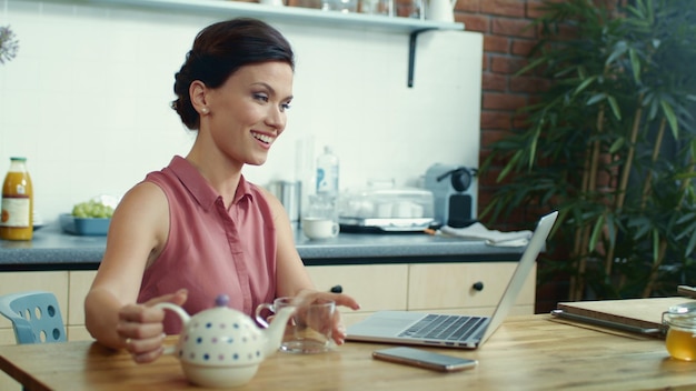 Mujer sirviendo té en una taza durante una videollamada