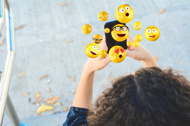 Mujer con smartphone enviando emojis.