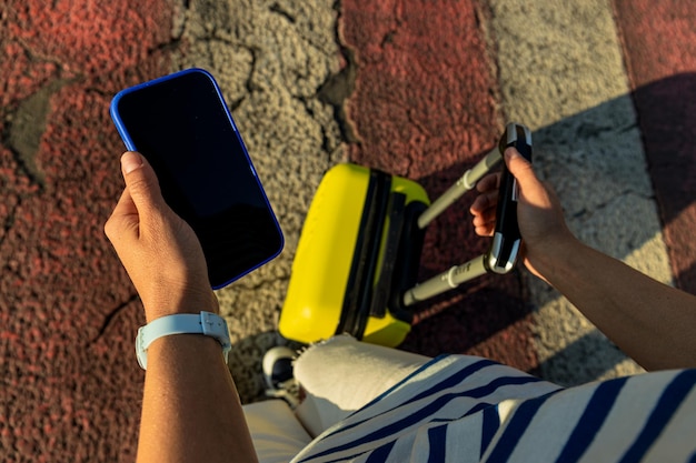 Mujer con smartphone y maleta amarilla en la carretera de la ciudad