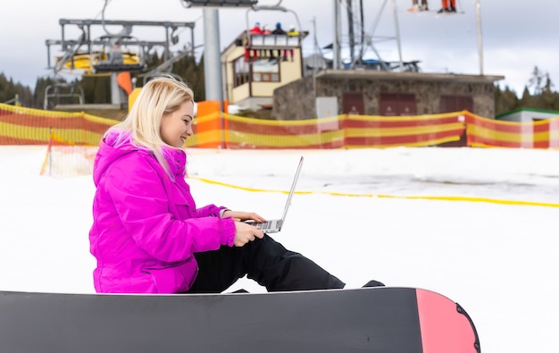 Mujer snowboarder portátil de trabajo en las montañas de invierno