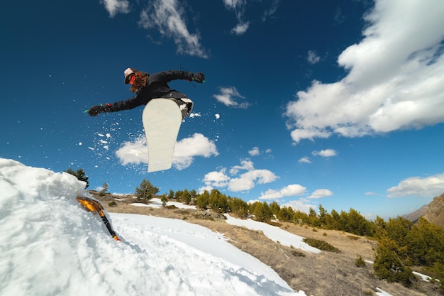 Foto mujer snowboarder saltando de un trampolín de patada de la nieve en un día soleado en las montañas