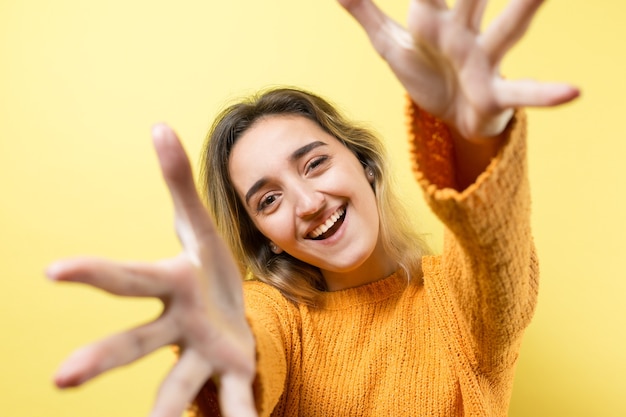 Una mujer sobre un fondo amarillo tira de sus manos hacia adelante, sonriendo, feliz.