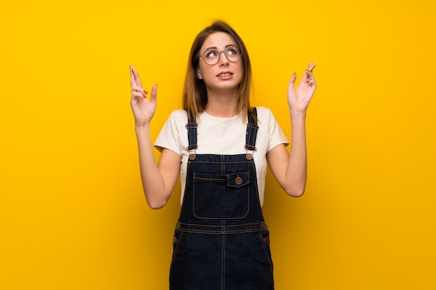 Mujer sobre muro amarillo con dedos cruzándose y deseando lo mejor.