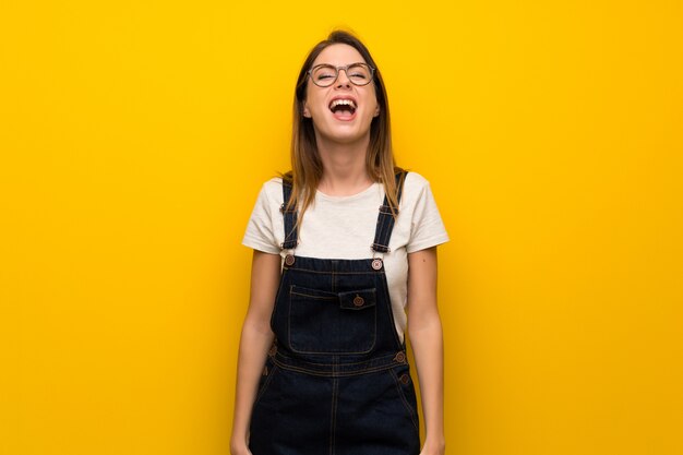 Mujer sobre muro amarillo gritando al frente con la boca abierta