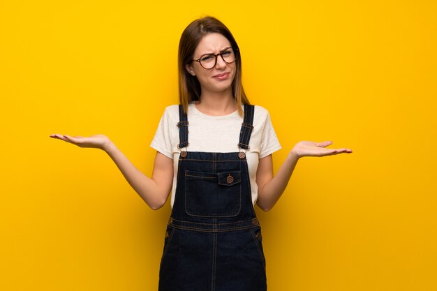 Mujer sobre muro amarillo infeliz porque no entiende algo.