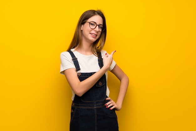 Mujer sobre pared amarilla apuntando hacia atrás