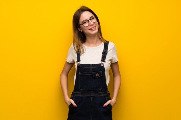 Mujer sobre pared amarilla con gafas y sonriendo